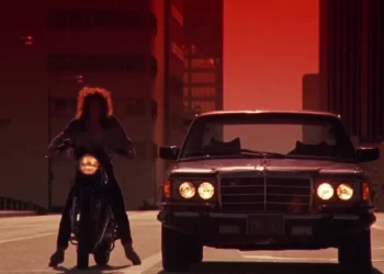 Motorcycle rider next to car at sunset.